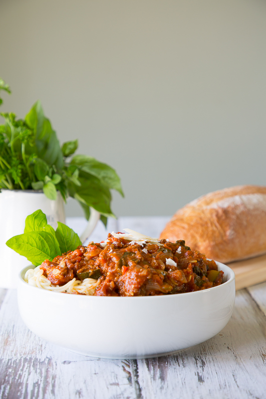 large bowl of spaghetti with bread and herbs in background