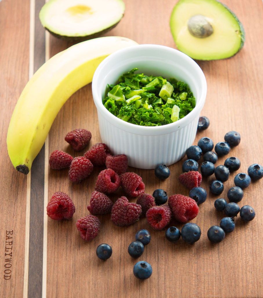 berries, banana, kale, and avocado on cutting board